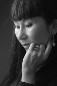 Black and white photograph of Amy Tan with eyes downcast and a hand on her jaw