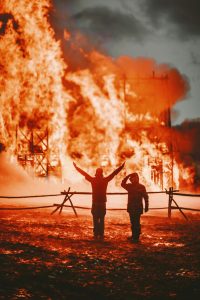 Two men standing in front of a large fire.